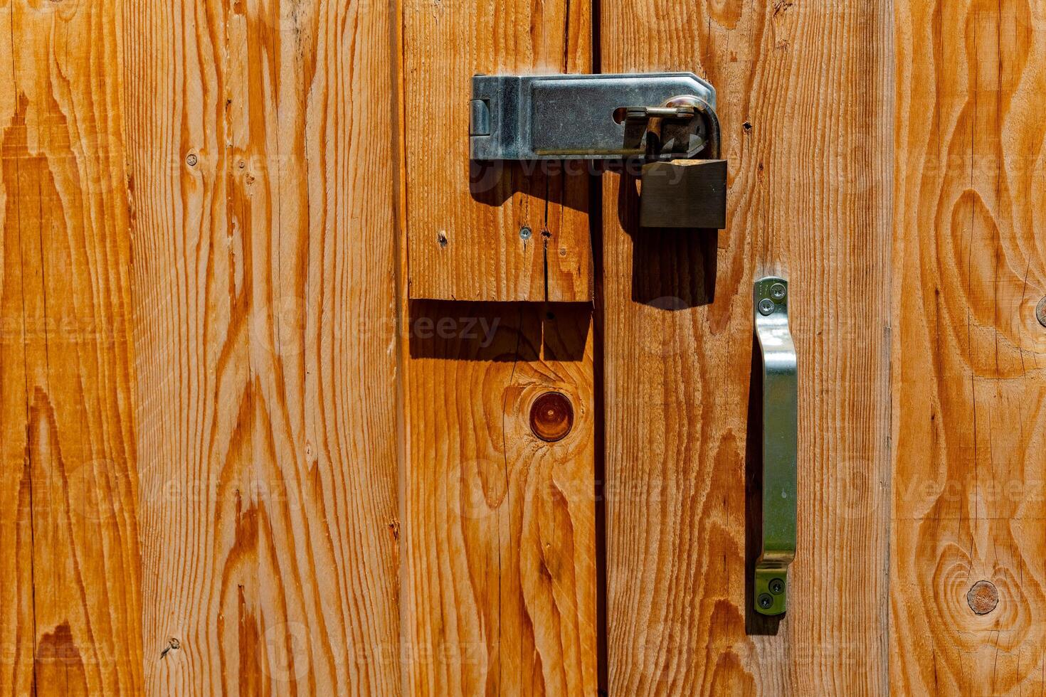 Bold wooden door with padlock and metallic handle illuminated by sunlight creates a rustic atmosphere in a countryside setting photo