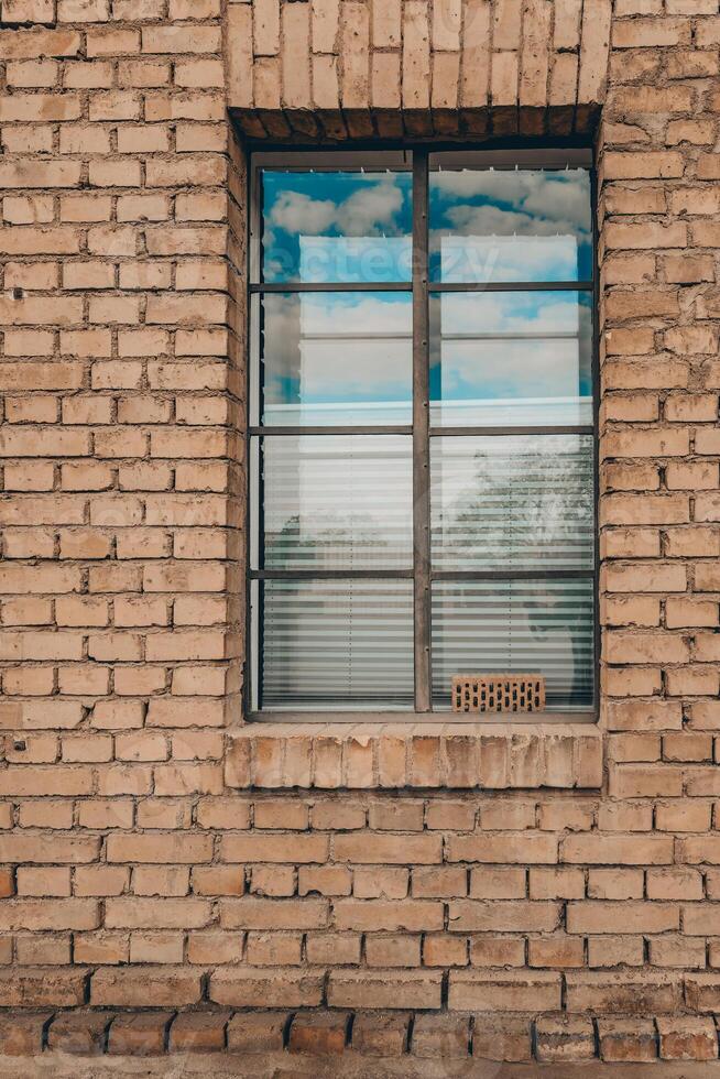 Reflections of clouds shimmer through a window framed by warm, textured brick in a peaceful rural setting during the afternoon photo