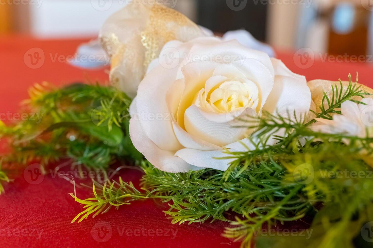 Beautiful white rose elegantly arranged on a vibrant red tablecloth with lush greenery, creating a stunning decor for a festive occasion photo