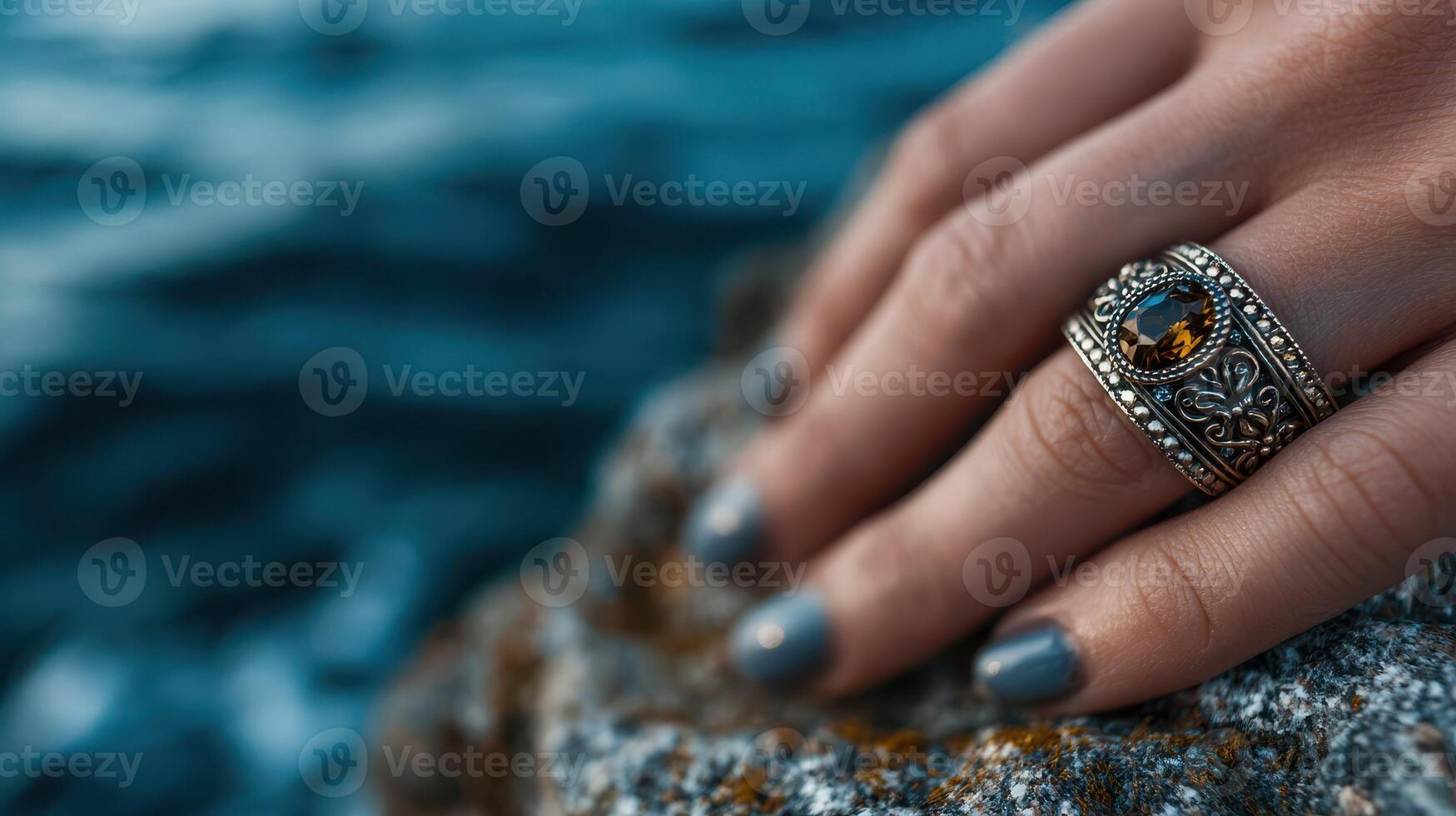 Hand resting on a rock with an ornate ring by the ocean during sunset hours photo