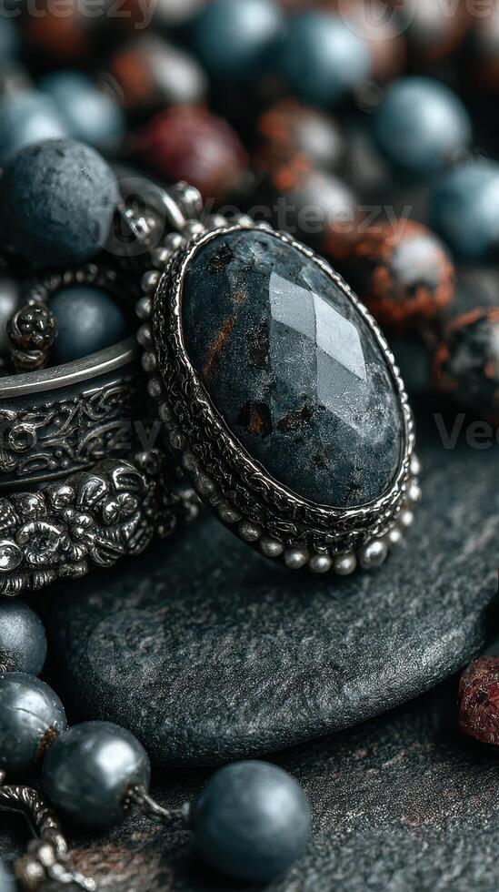 Elegant jewelry arrangement featuring a dark gemstone and colorful beads on textured stone surface photo