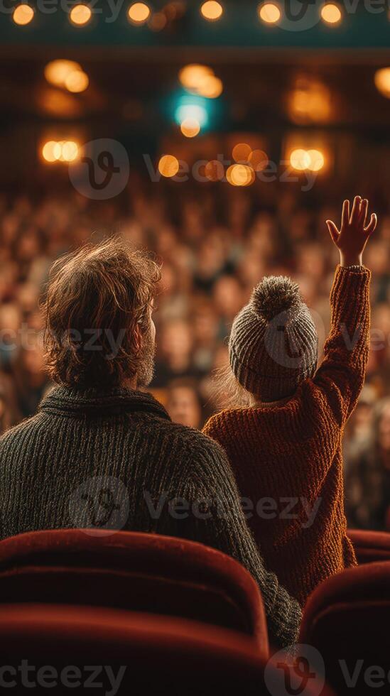 Parent and child enjoying a performance at a theater with excited audience in the background photo
