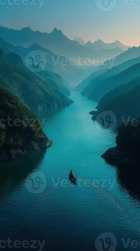 Misty mountains and calm river with a solitary boat navigating at dawn photo