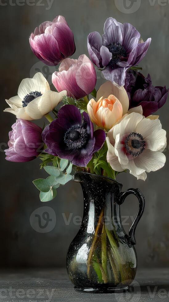 Colorful anemones arranged in a vintage black pitcher on a solid background in a softly lit setting photo