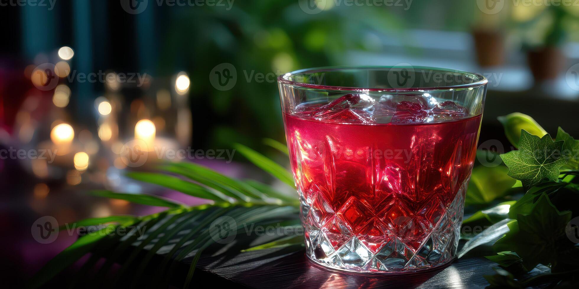 Refreshing red drink served in a crystal glass with ice and candles in the background photo