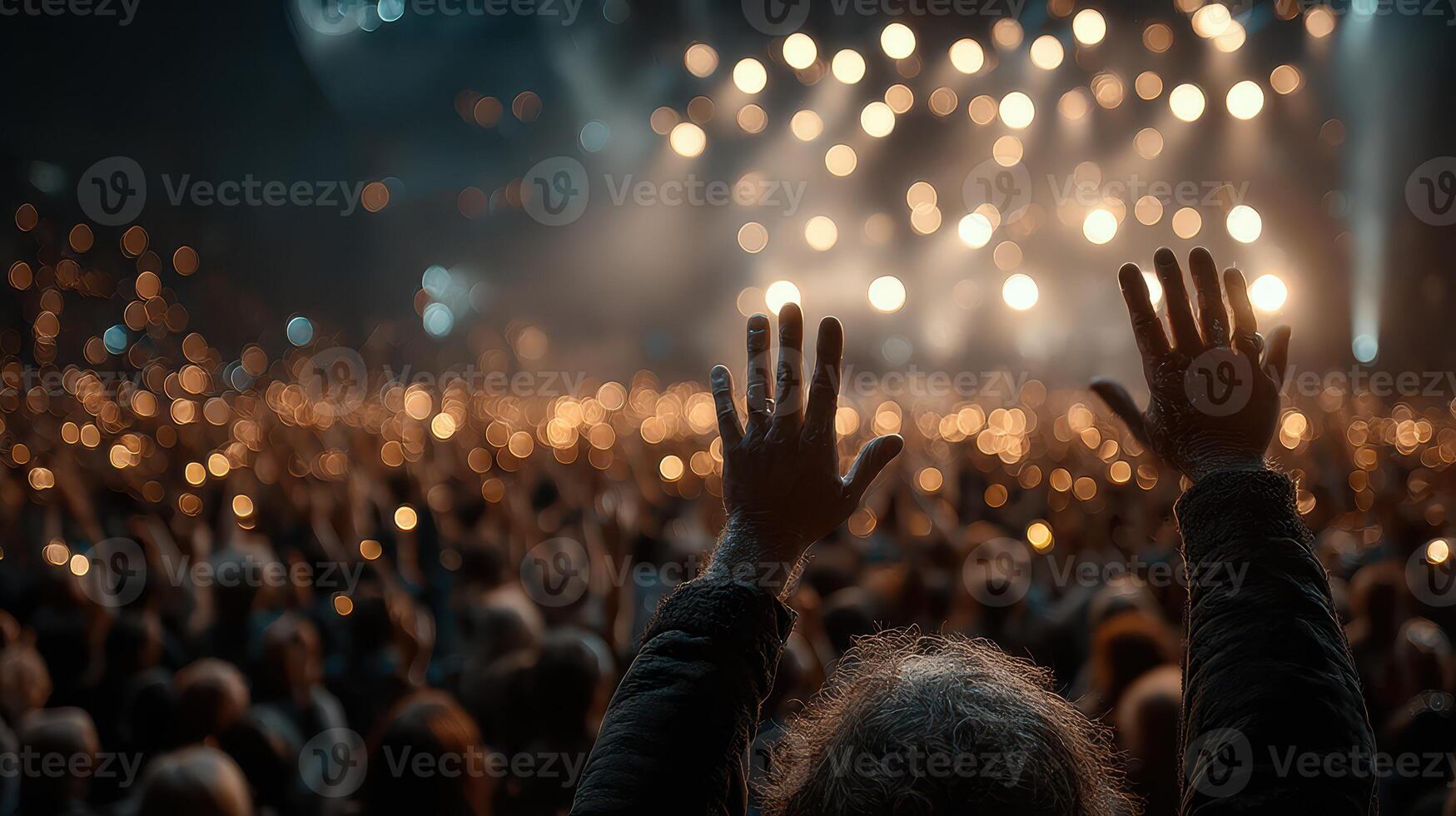 Crowd enjoys live concert with raised hands and glowing lights in the background during an evening performance photo