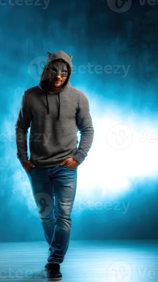 Stylish young man wearing a hooded sweater walking confidently in a dramatic blue-lit environment photo