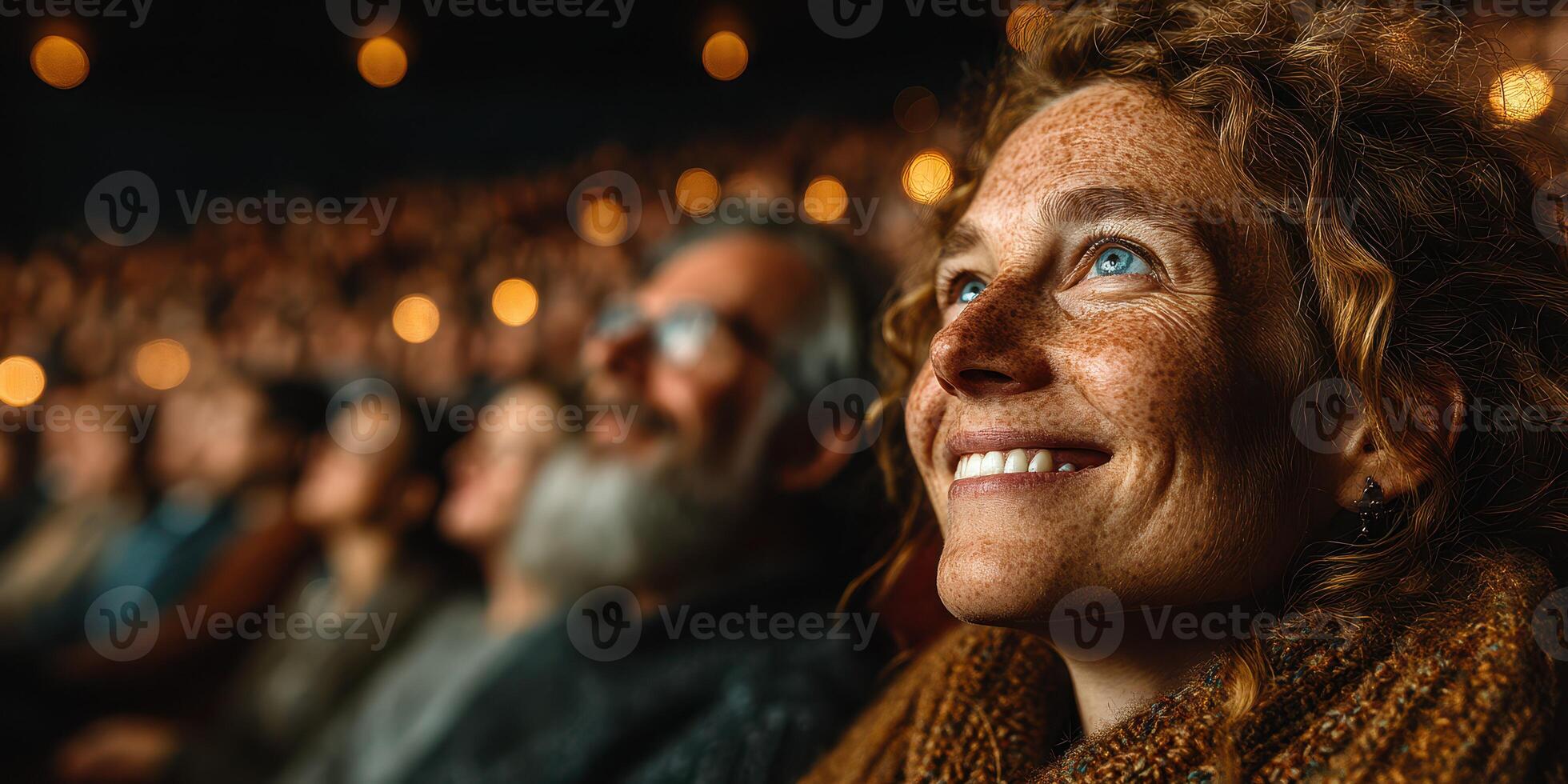 Audience member smiles with joy while watching a performance in a theater filled with warm lighting at night photo