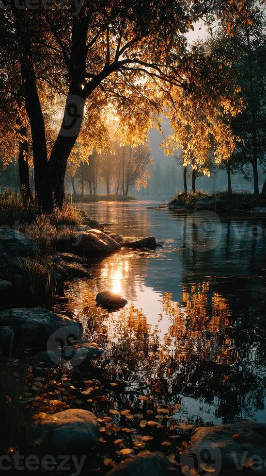 Golden sunlight filters through trees beside a tranquil river at dawn, illuminating the surrounding autumn foliage and water photo