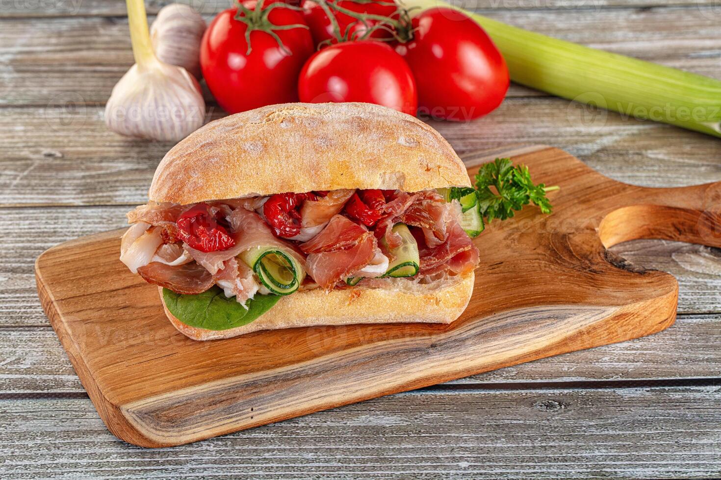 A sandwich on a cutting board with tomatoes and garlic photo