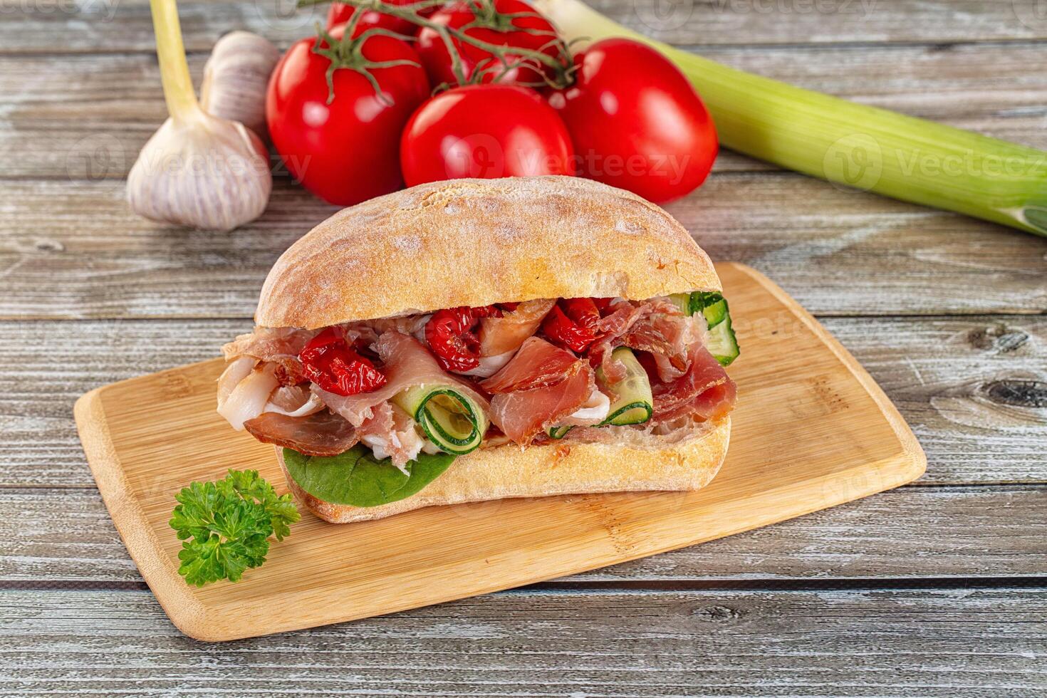 A sandwich on a wooden cutting board with tomatoes and garlic photo