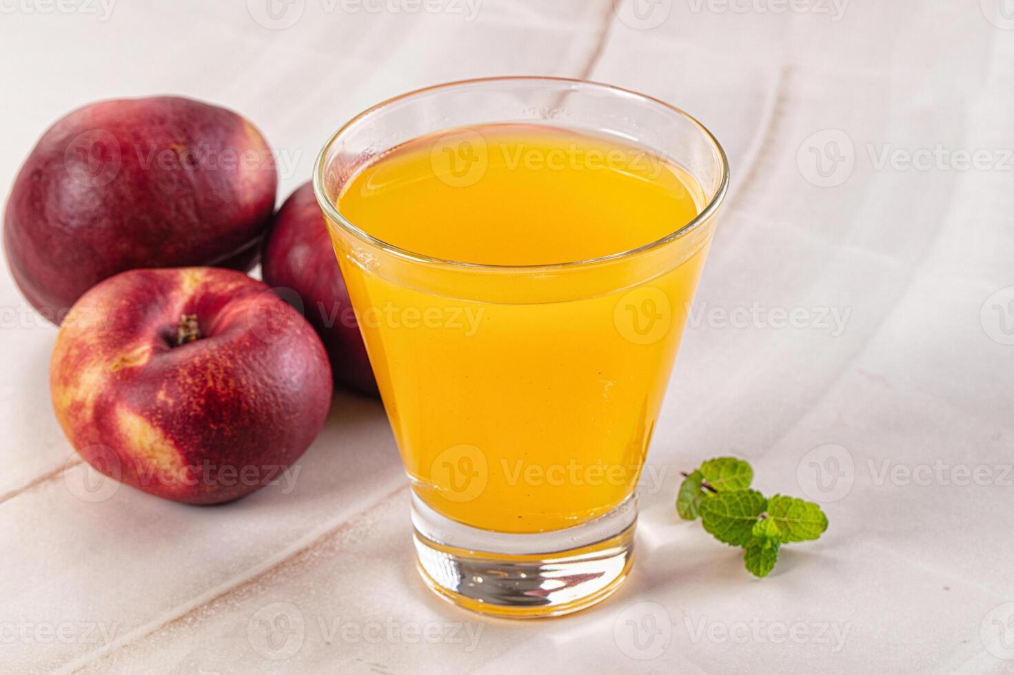 A glass of juice next to a peach and a leaf photo