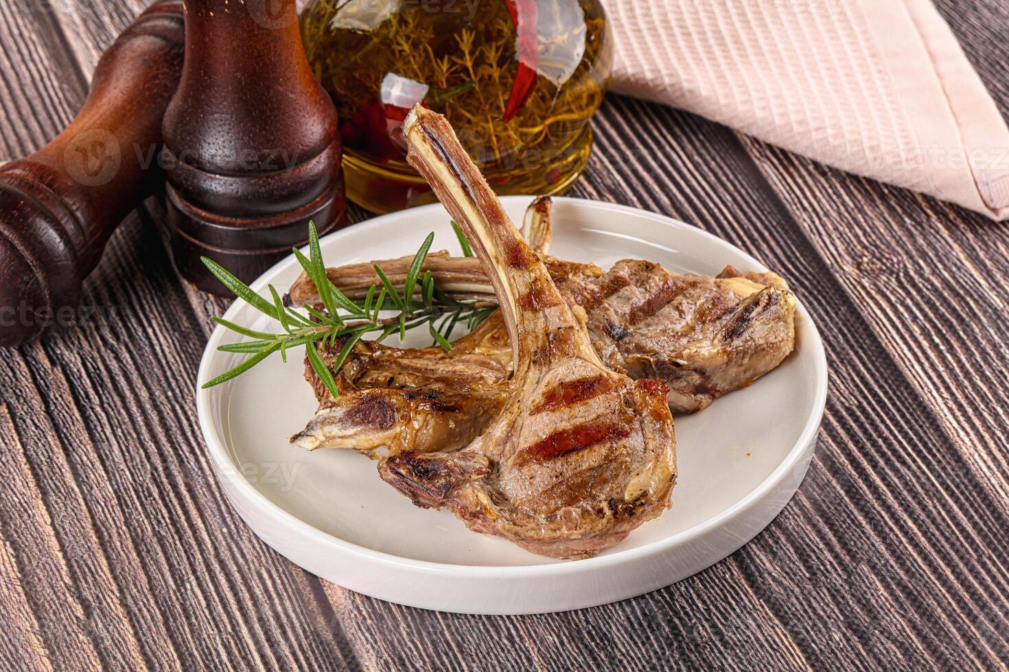Grilled lamb chops on a white plate with rosemary sprigs photo