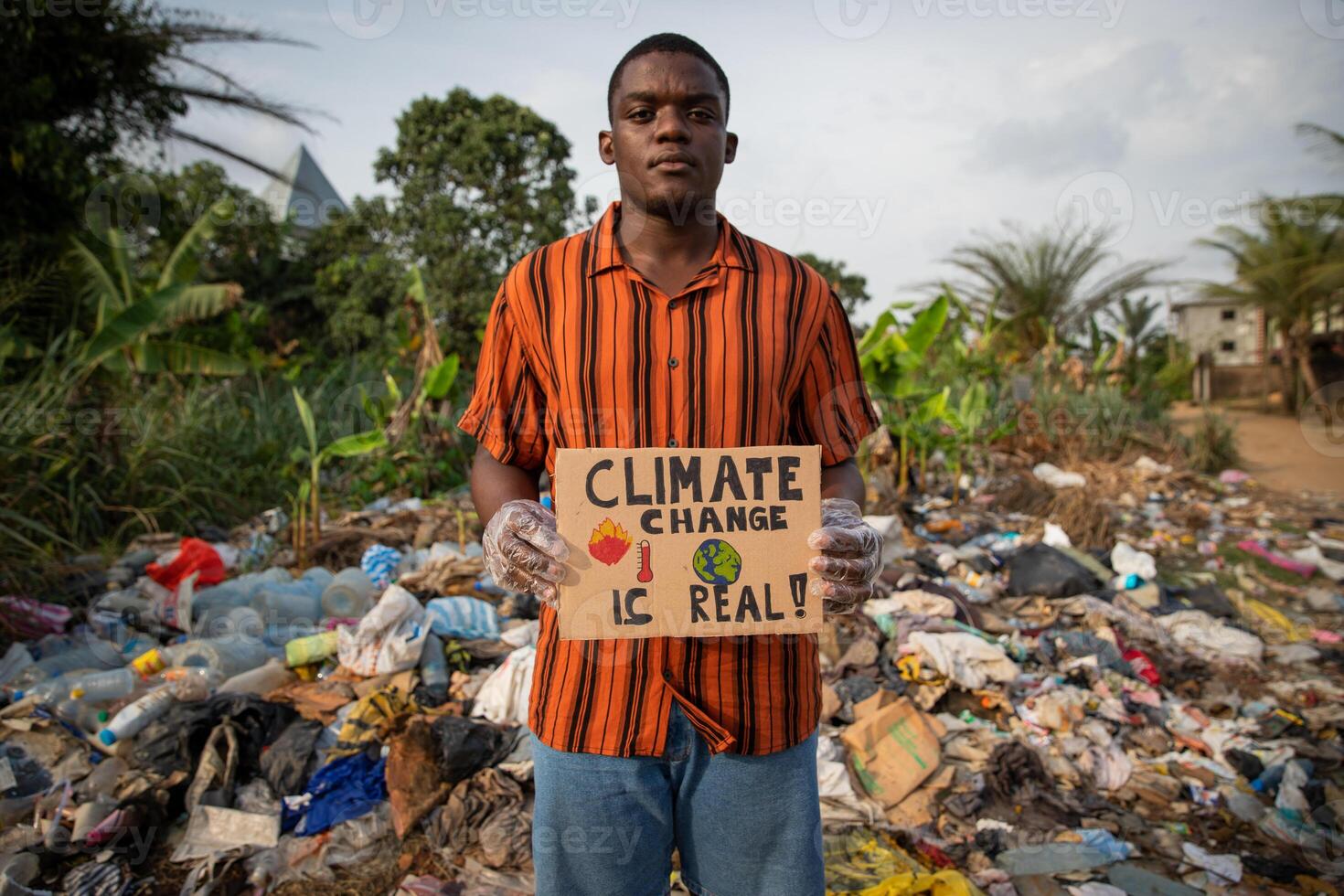 African boy holds a sign in his hand with the words climate change is real and protests in front of an illegal landfill photo