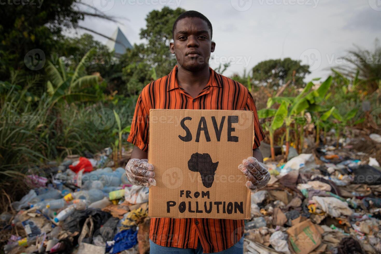 a boy holds a Save Africa from Pollution sign and stands by an illegal landfill. Protest against pollution in africa. photo