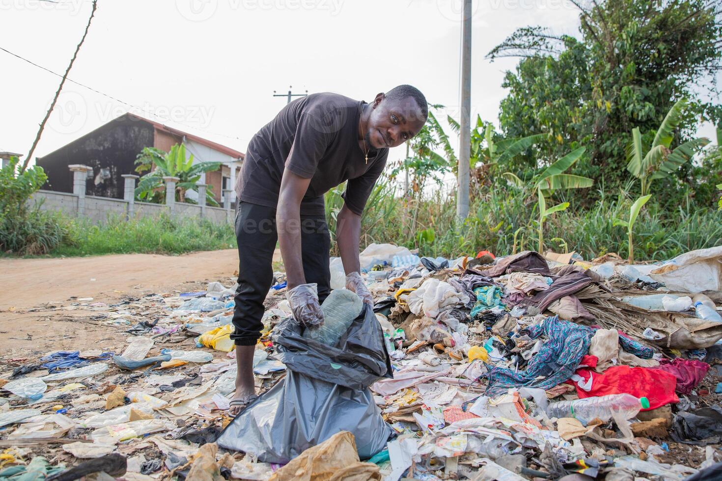 Young african man looks at the camera while collecting waste from the ground photo