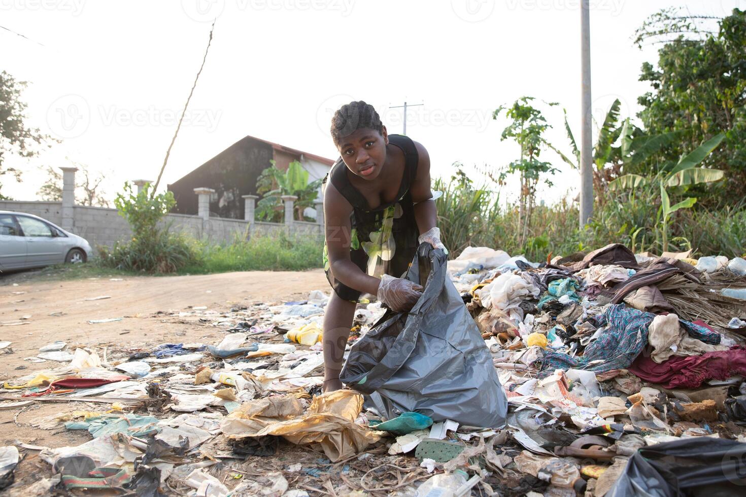 Young African girl picks up garbage thrown there in the open air. Pollution concept photo