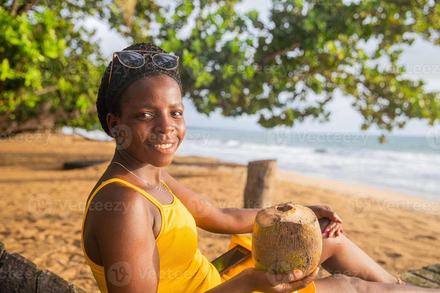 Beautiful girl enjoys her beach vacation sitting on the sand drinking coconut milk photo