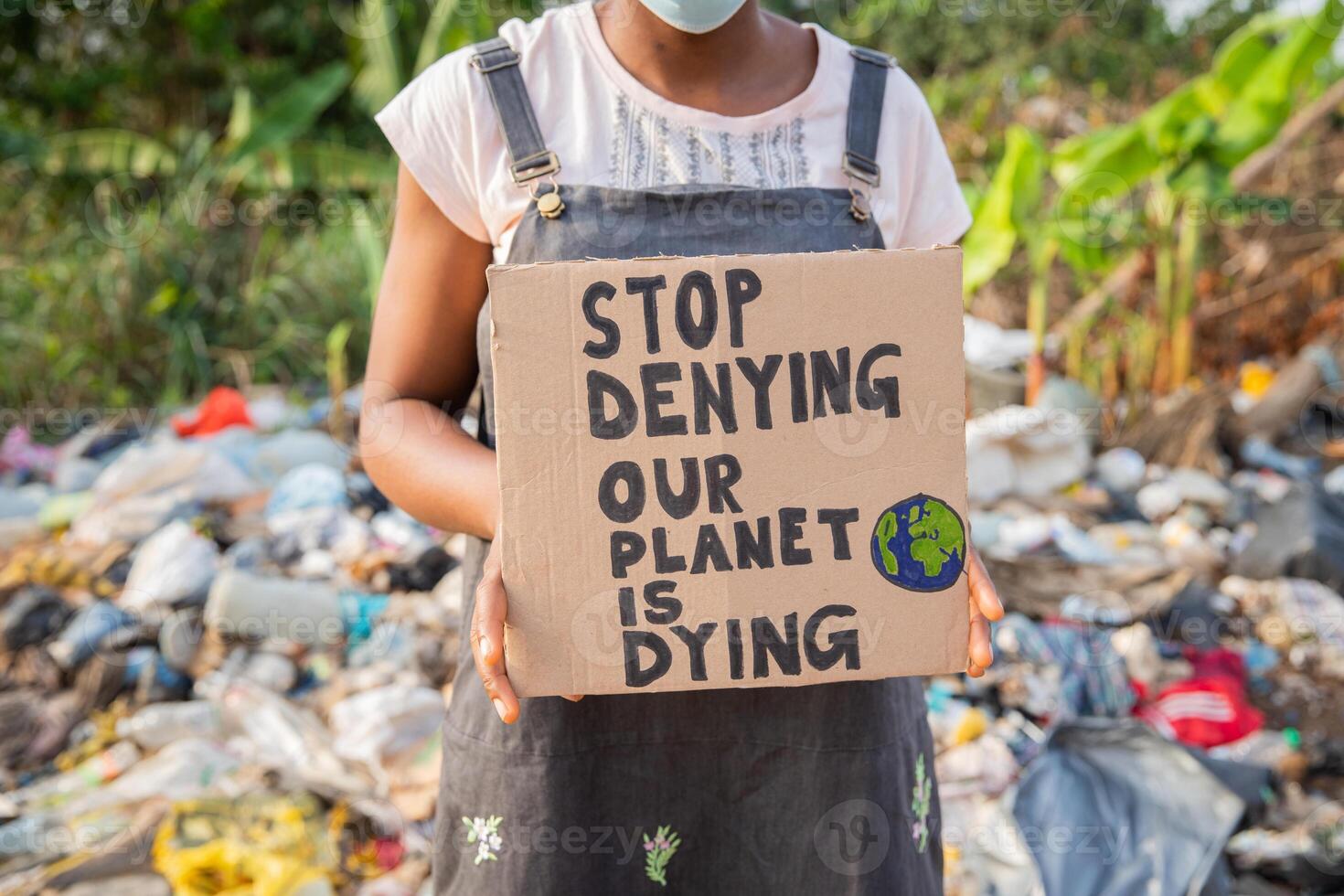 Closeup of a sign with written Stop denying our planet is dying held in the hand by a girl during a protest outside an illegal open-air landfill photo
