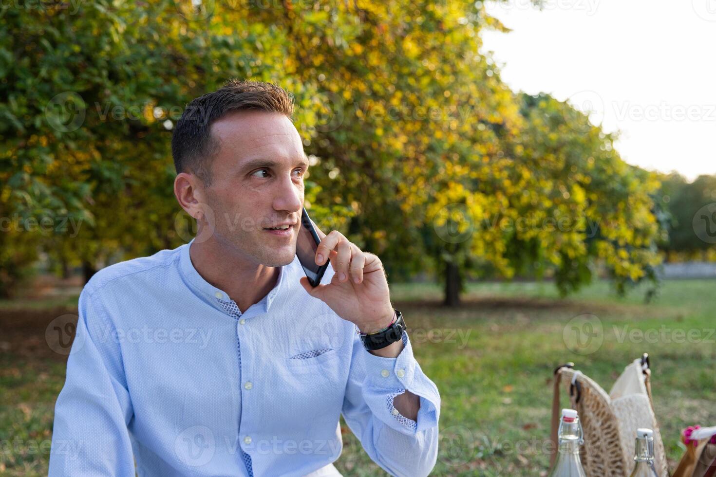 Young smiling man in his thirties while picnicking in the park makes a phone call photo