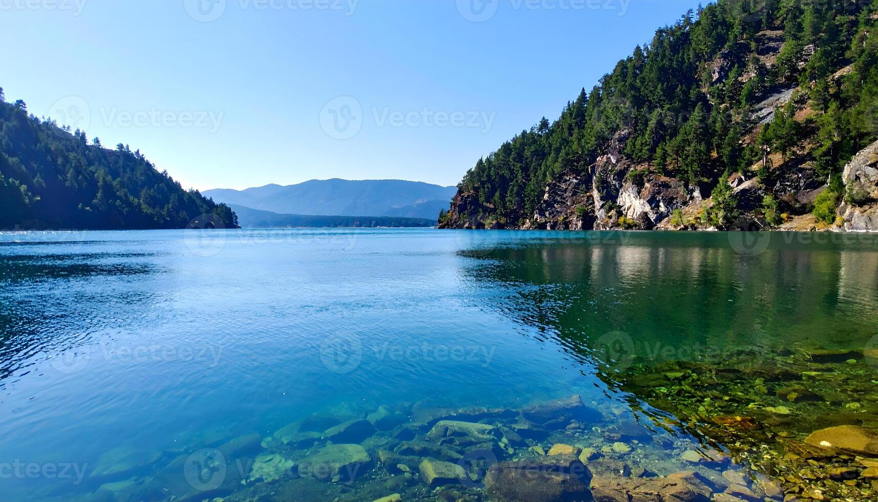Serene lake surrounded by lush green mountains under a bright blue sky photo