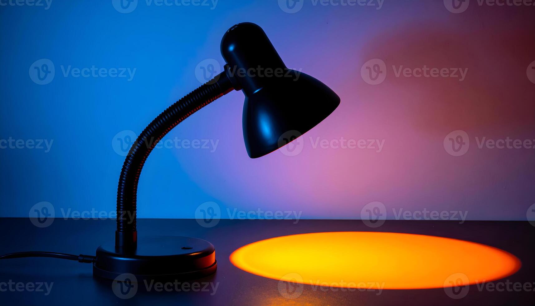 Black desk lamp with warm orange light against a colorful gradient background photo
