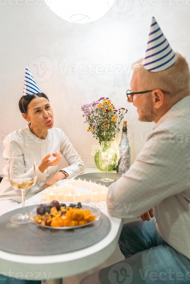 Here's a title attempting to follow all instructions. Couple Birthday Celebration Party Indoor. Mature adults celebrate birthday indoors with champagne, snacks, and party hats. photo