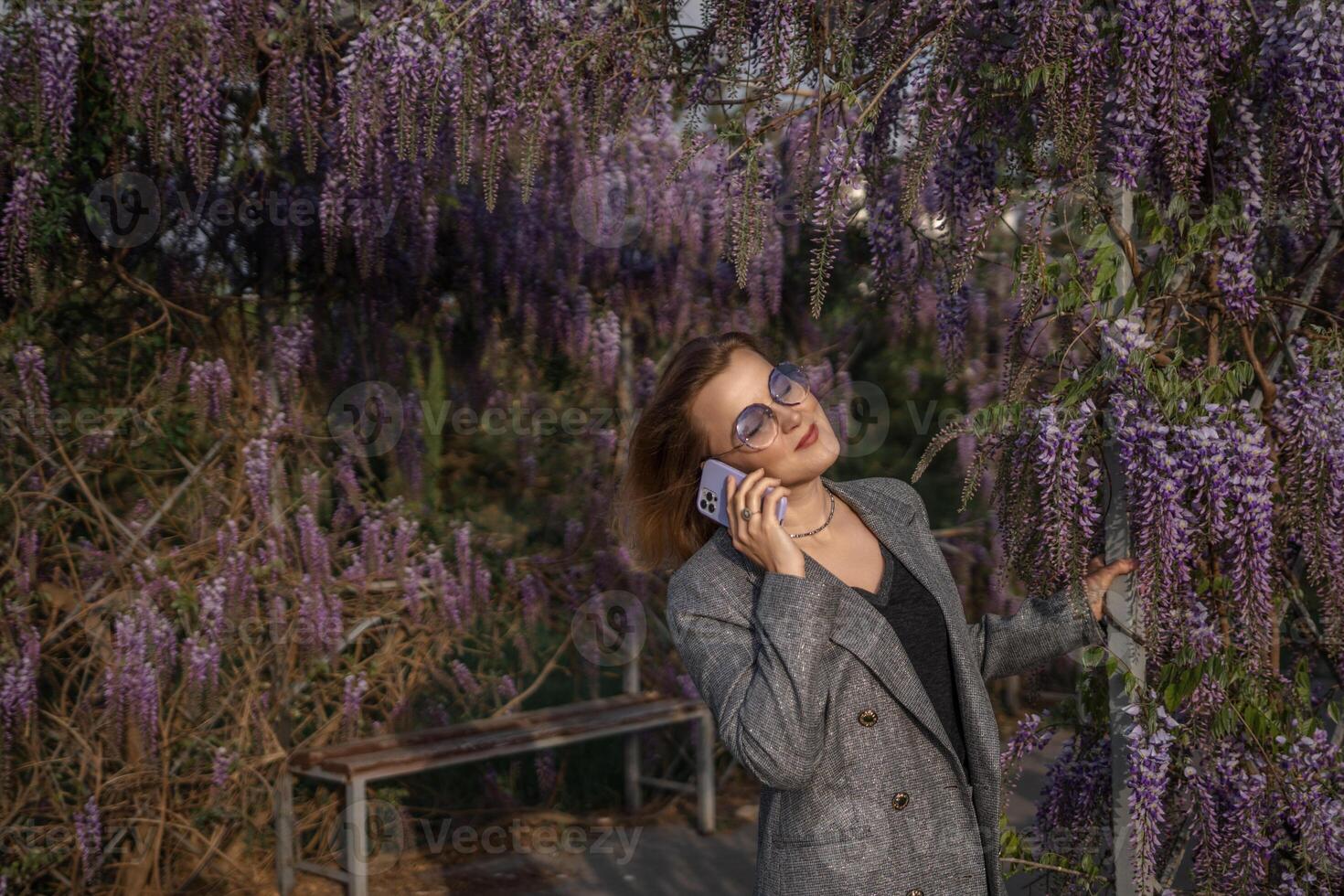 Wisteria, Woman, Phone Call. A woman talks on a phone call standing in a garden with a wisteria vine. photo