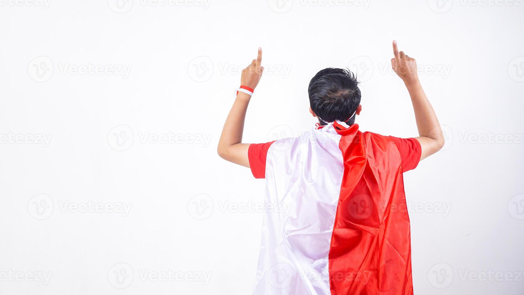 Rear view of Indonesian man celebrate Indonesia independence day on August 17 by tied the Indonesian flag behind his back and raising his forefinger to the sky isolated on white background photo
