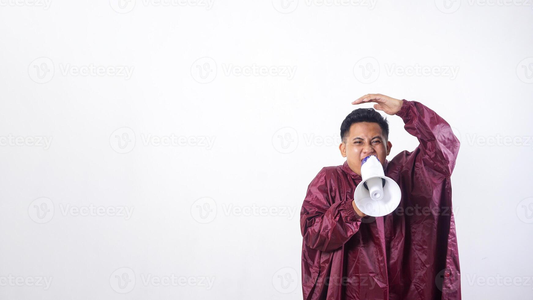 Asian man in red raincoat holds megaphone and covering his head with hand to shield face from rain isolated on white background photo