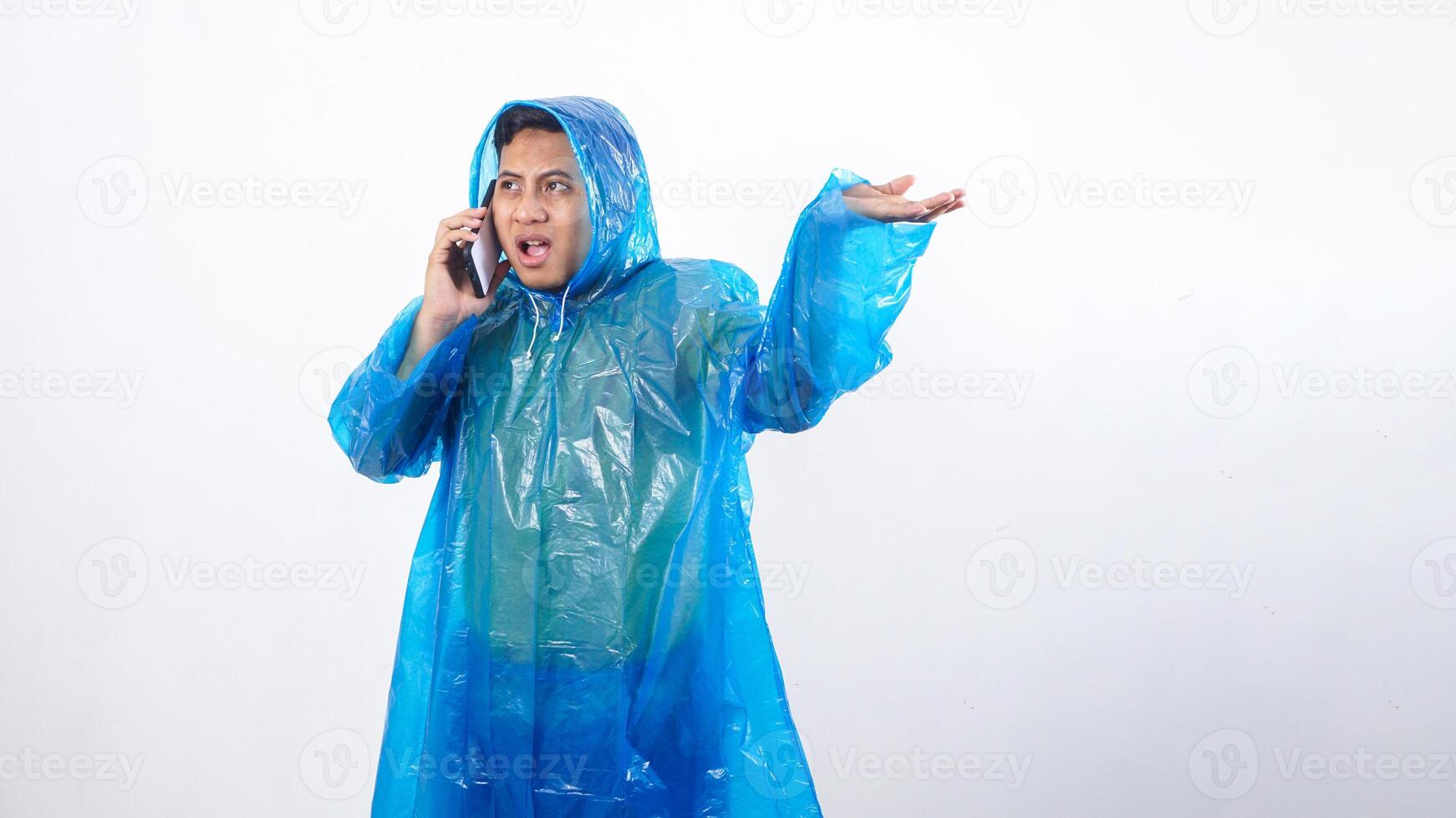 Asian young man in blue raincoat checking if it raining whit his hand while talking on the phone isolated on white background photo