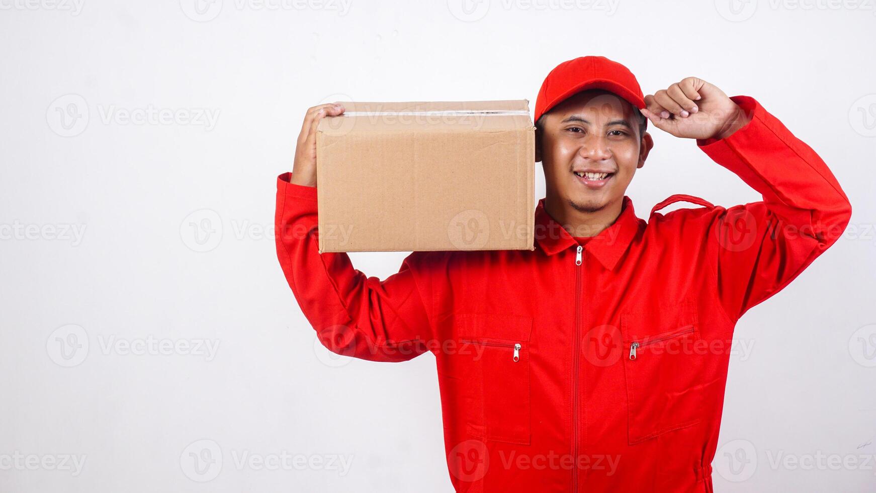 Delivery man in red uniform carrying stack of package box parcel on his shoulder while touching his cap visor isolated on white background photo