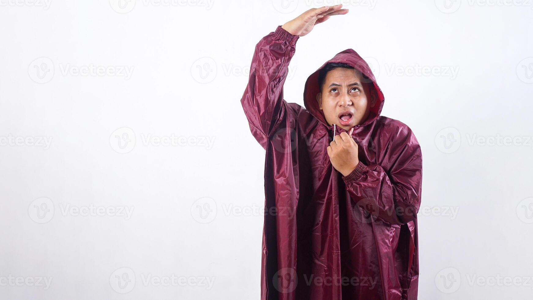 Worried Asian man in red raincoat covering his head with hand to shield face from rain isolated on white background photo