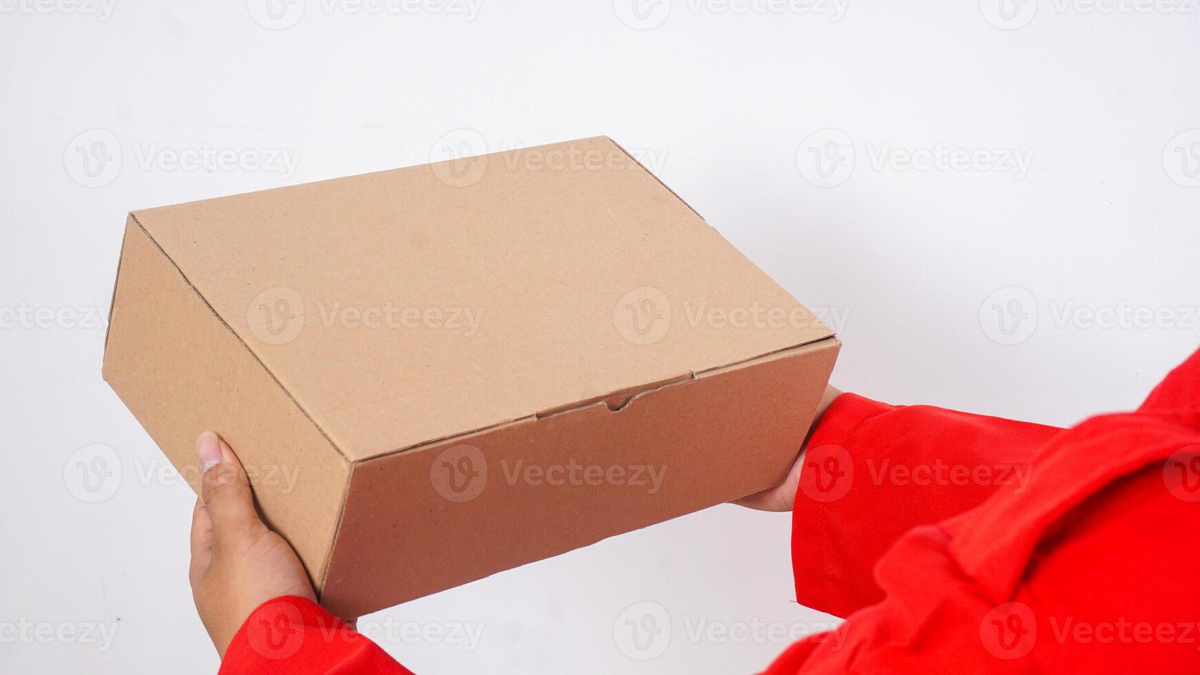 Close up of delivery man in red uniform holds a package box parcel isolated on white background photo
