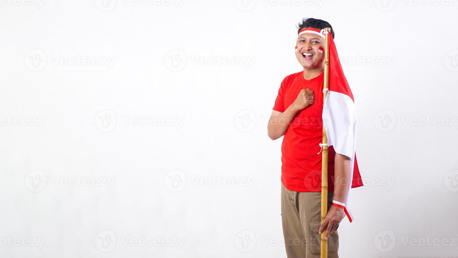 Portrait of Happy Indonesian man celebrate Indonesia independence day on August 17 by holding the Indonesian flag and put his clenched hand in front of his chest isolated on white background photo