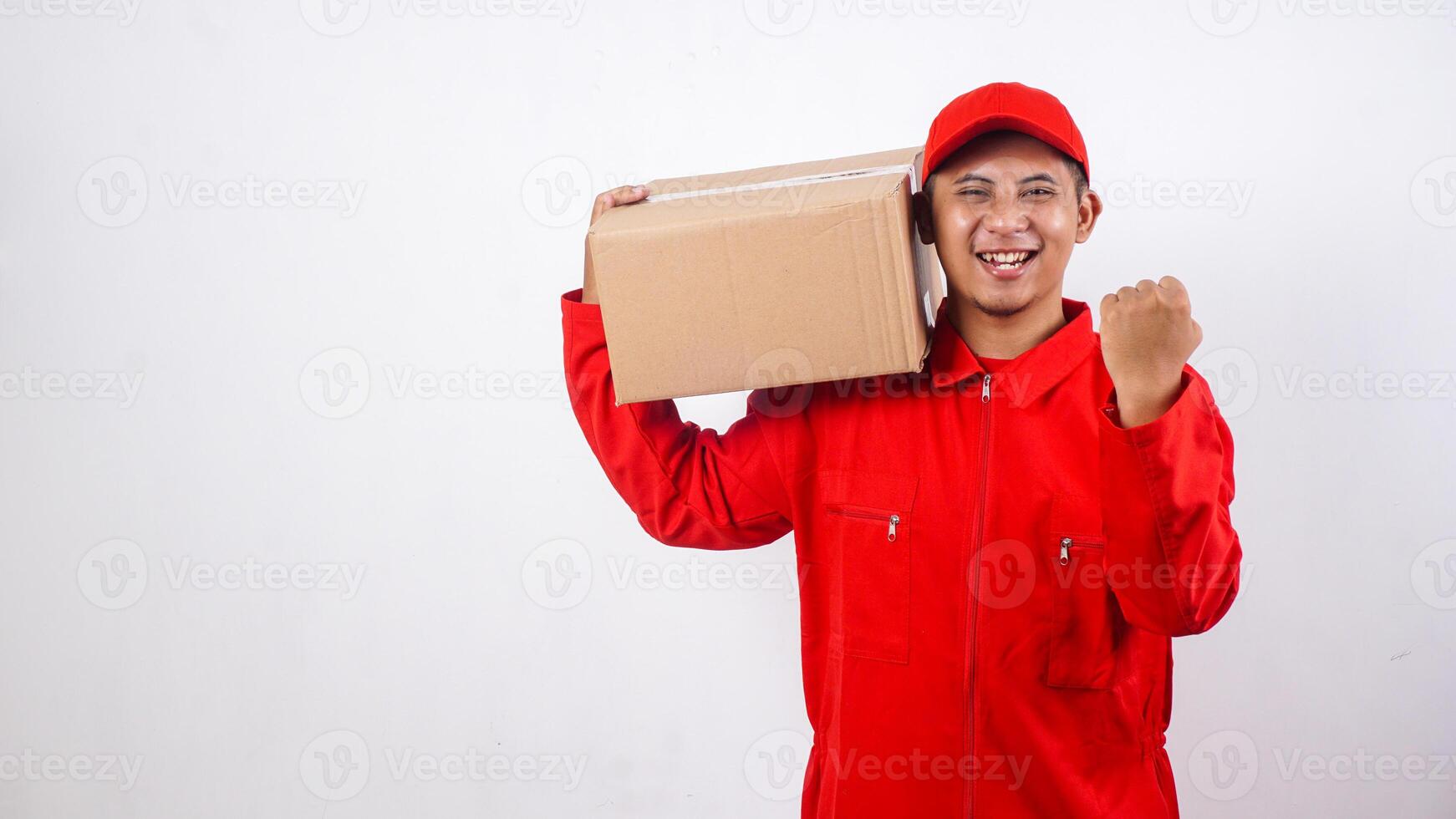 Delivery man in red uniform carrying stack of package box parcel on his shoulder and showing yes gesture to celebrate win victory isolated on white background photo