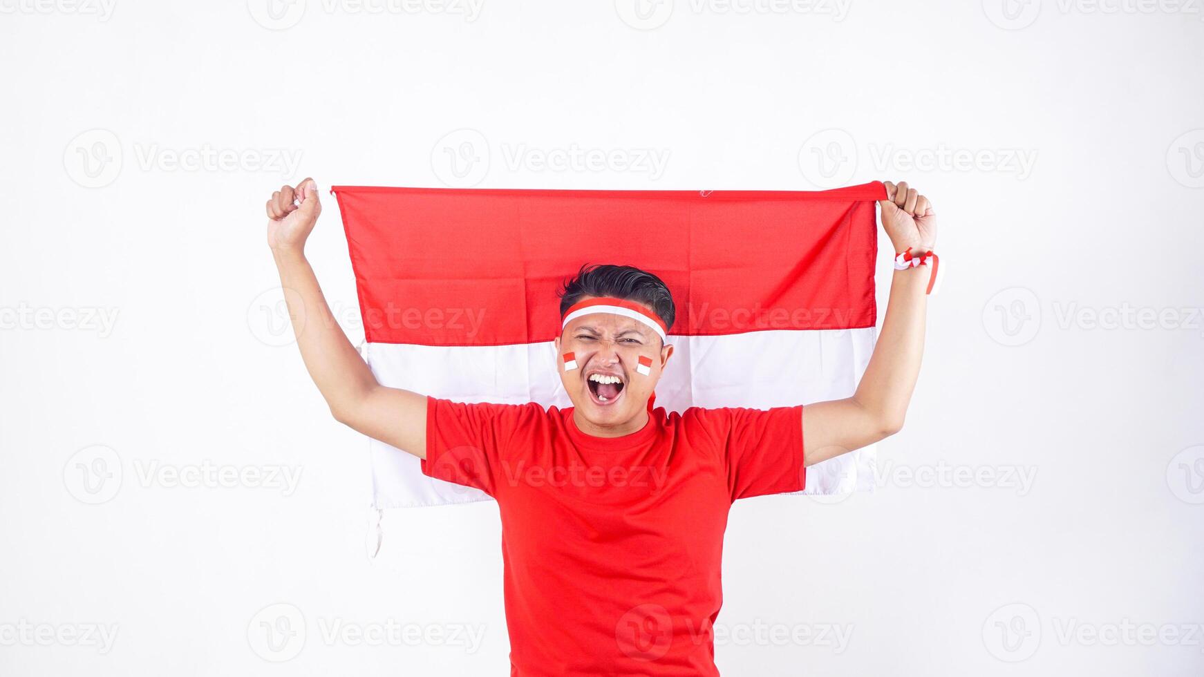Excited Indonesian man celebrate Indonesia independence day on August 17 by holding the Indonesian flag high behind his back isolated on white background photo