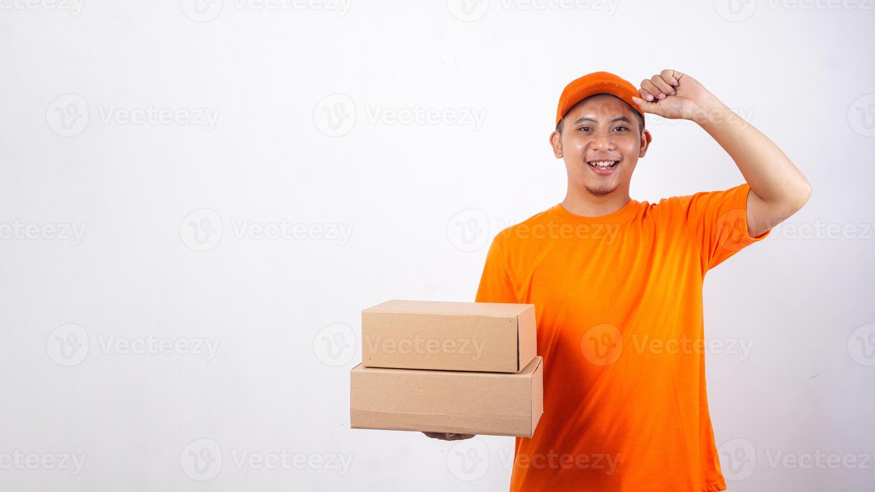 Asian deliveryman in orange t-shirt uniform with package boxes parcel and touching his cap visor isolated on white background photo