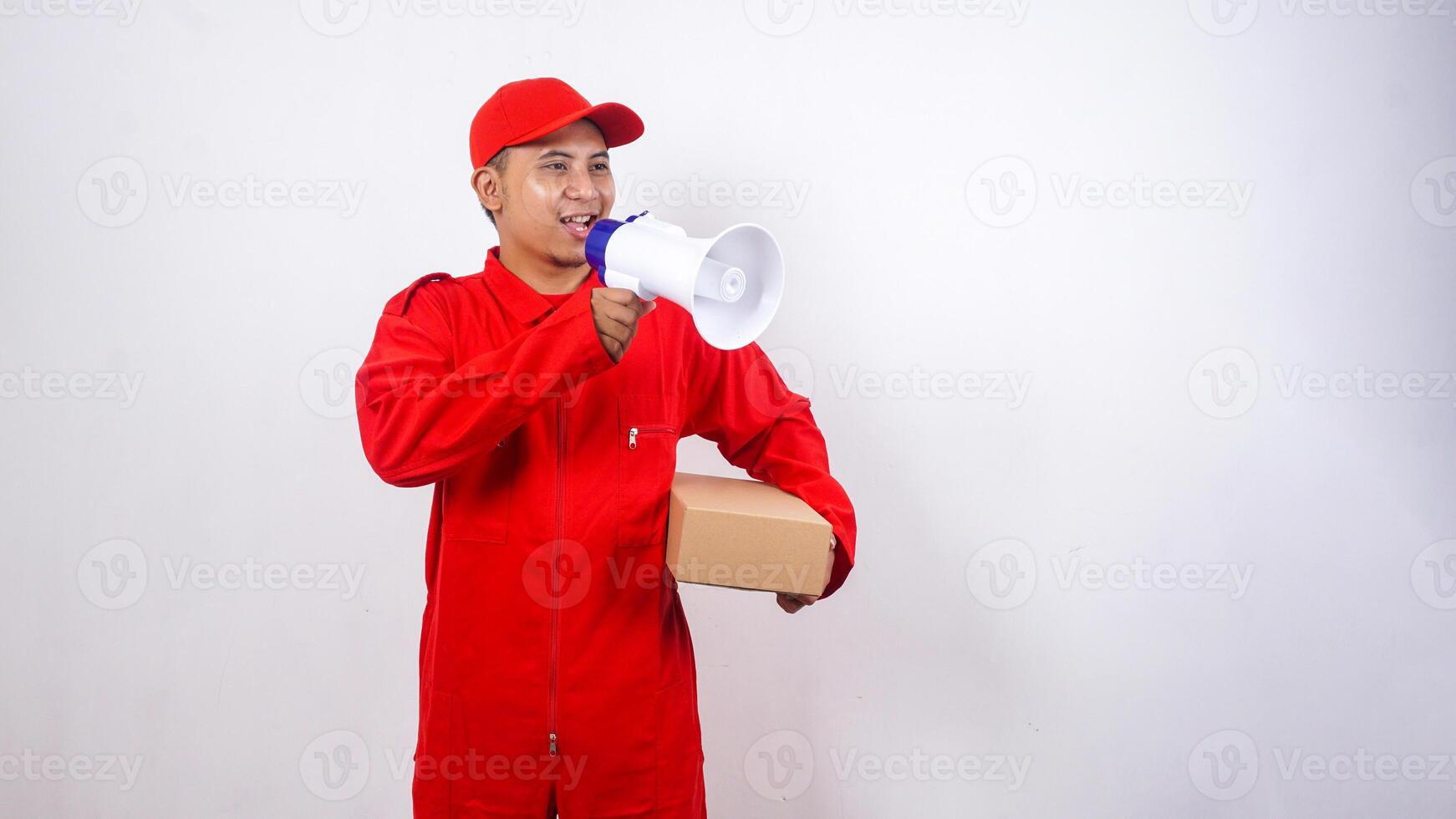 Portrait of Asian Delivery man in red uniform carrying a package box parcel while talk using megaphone isolated on white background photo