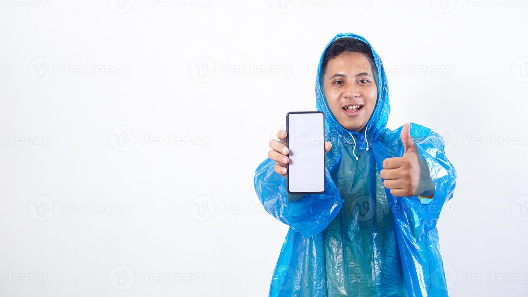 Asian young man in blue raincoat showing smartphone mock up with blank screen and raising thumb up isolated on white background photo