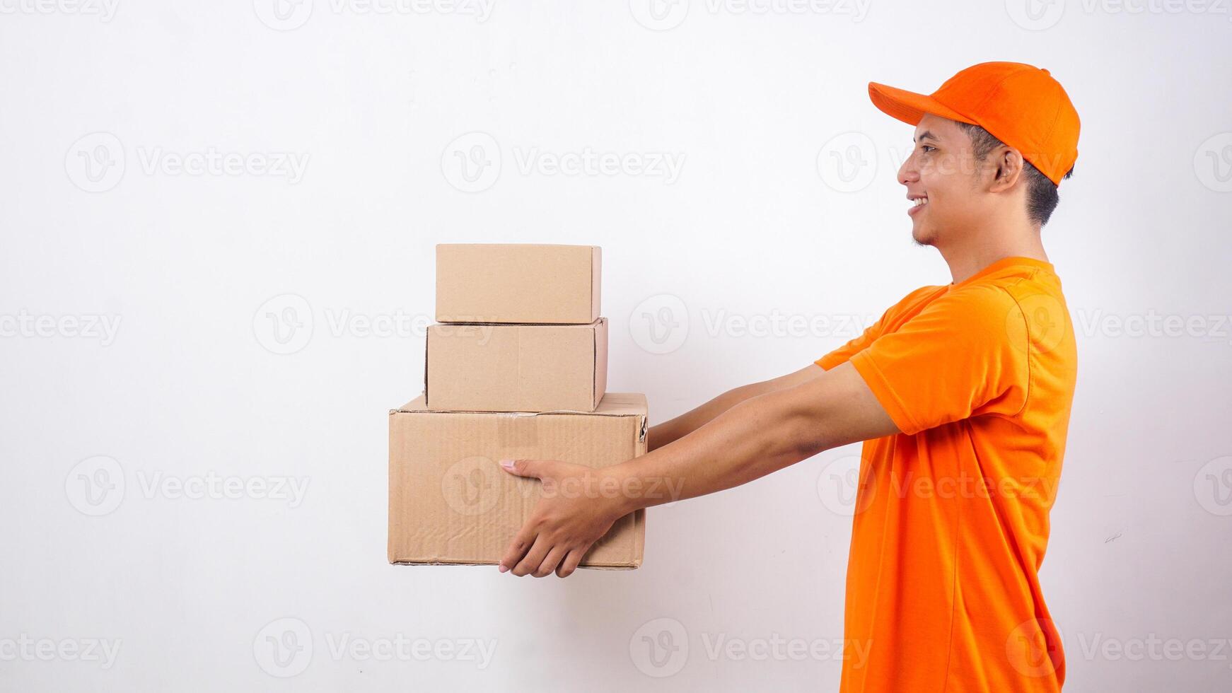 Side view of Asian deliveryman in orange t-shirt uniform giving stack of package boxes parcel to customer isolated on white background photo