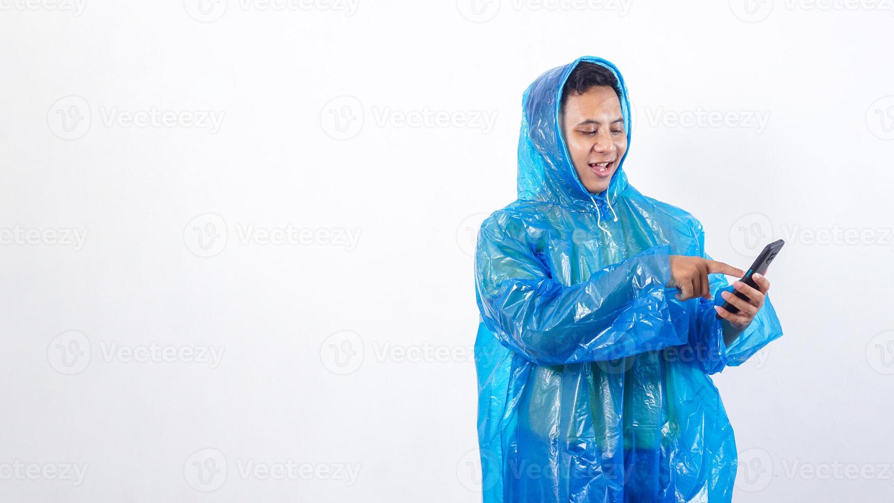 Asian young man in blue raincoat pointing at smartphone screen isolated on white background photo