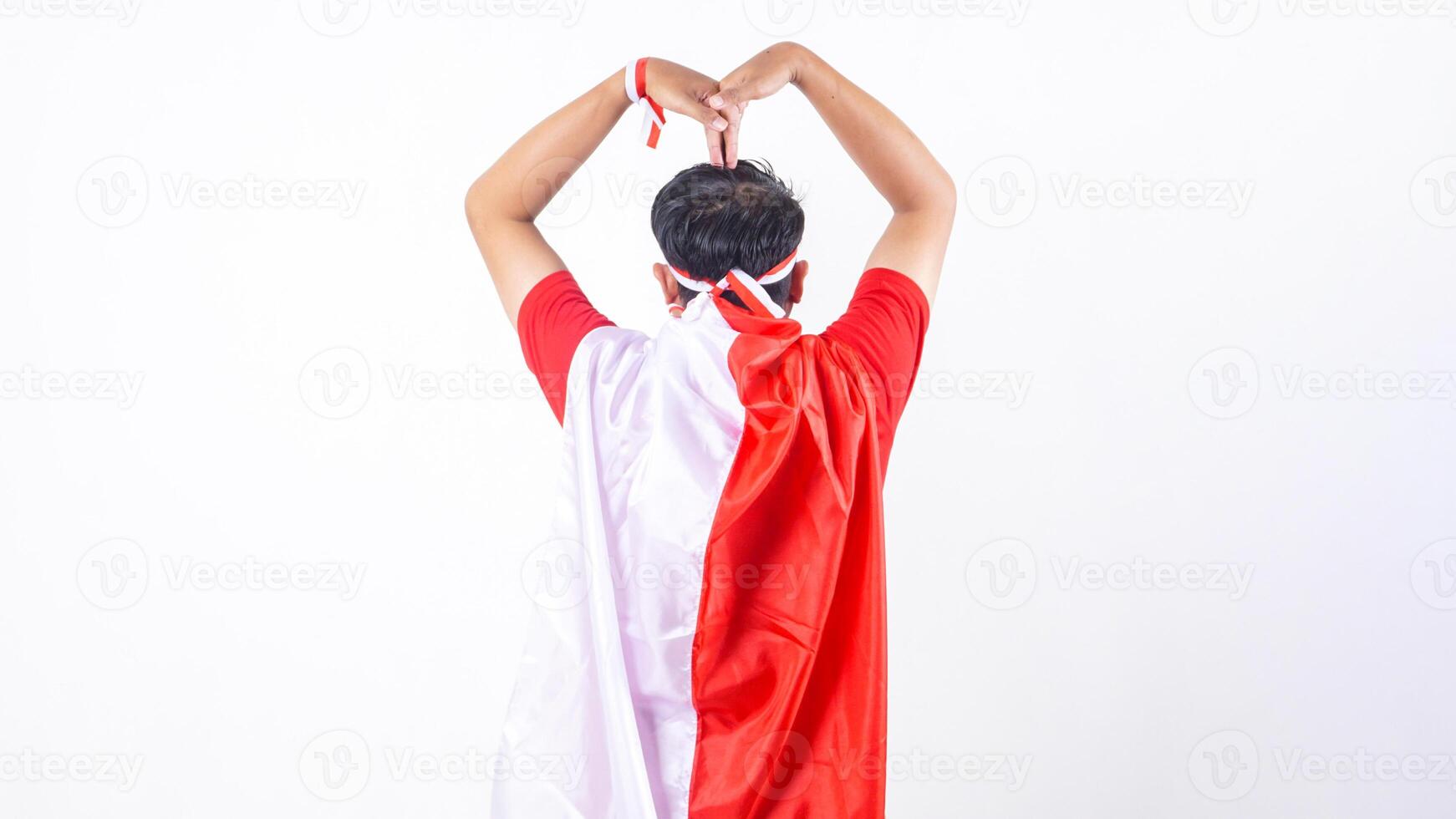 Rear view of Indonesian man celebrate Indonesia independence day on August 17 by tied the Indonesian flag behind his back and doing heart pose isolated on white background photo
