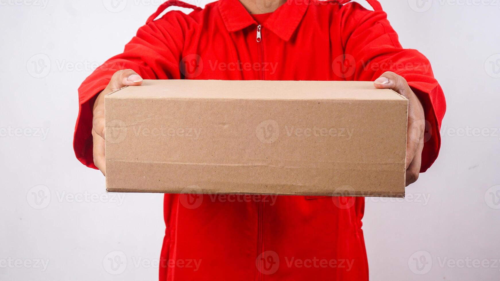 Close up of delivery man in red uniform holding a package box parcel to give to customer isolated on white background photo