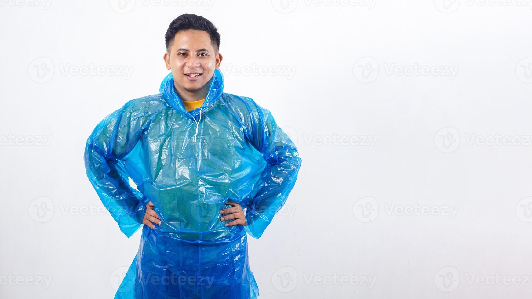 Asian young man in rain poncho standing with hands on his hips isolated on white background photo
