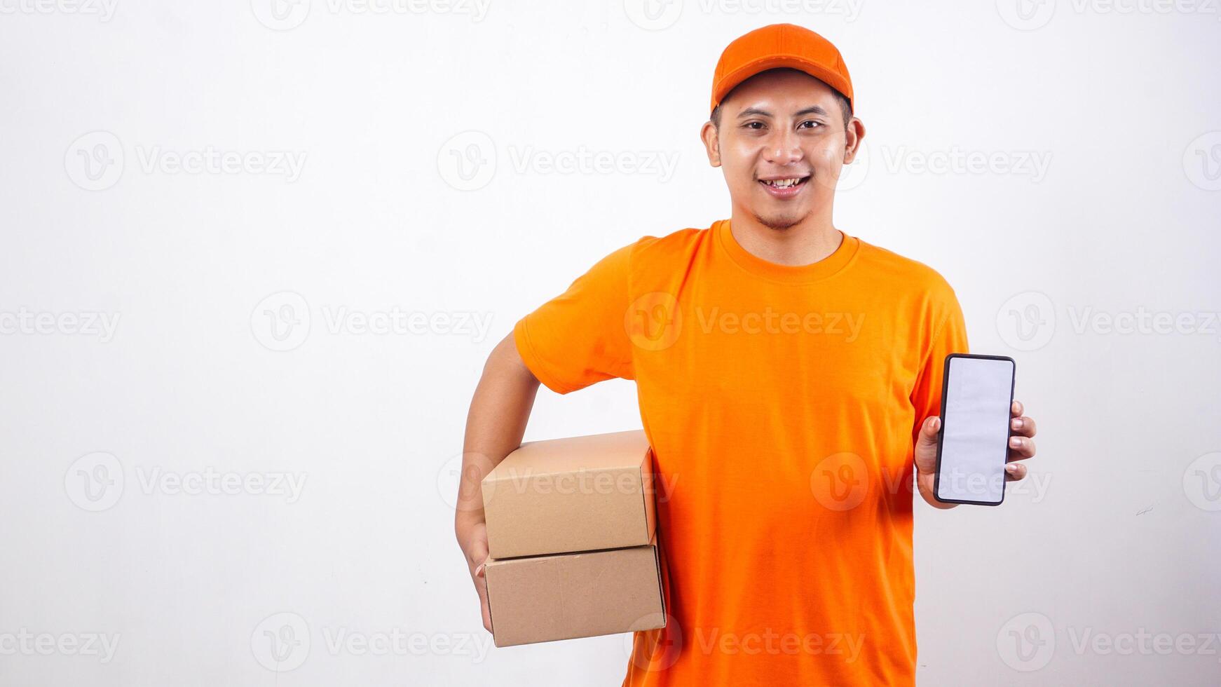 Asian Delivery man in orange t-shirt carrying package boxes parcel while showing a smartphone with blank screen isolated on white background photo