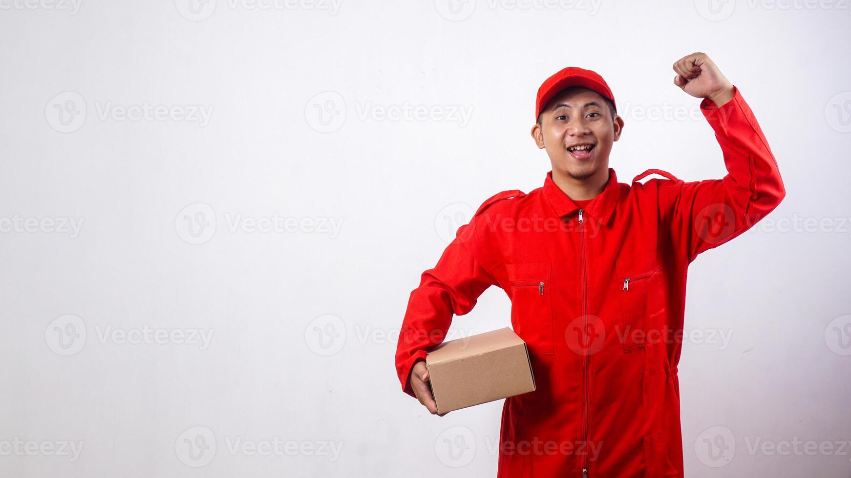 Delivery man in red uniform holding cardboard parcel box and raising clenched fist isolated on white background photo
