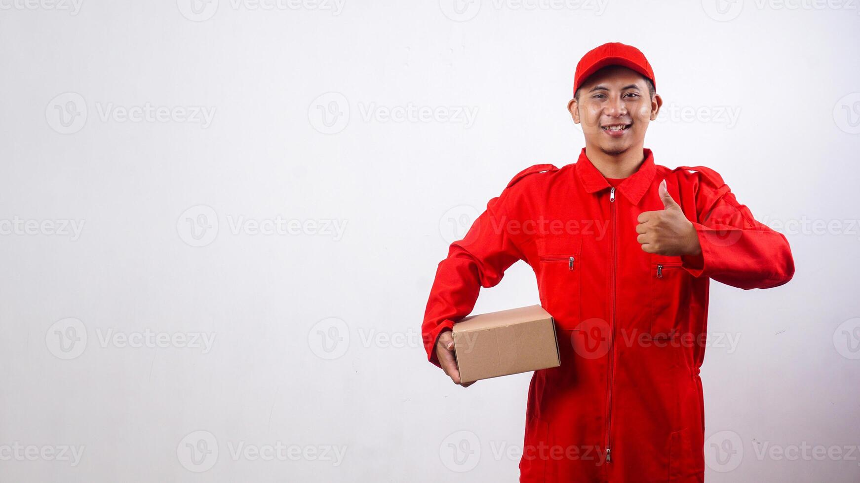 Delivery man in red uniform holding cardboard parcel box and showing thumb up isolated on white background photo