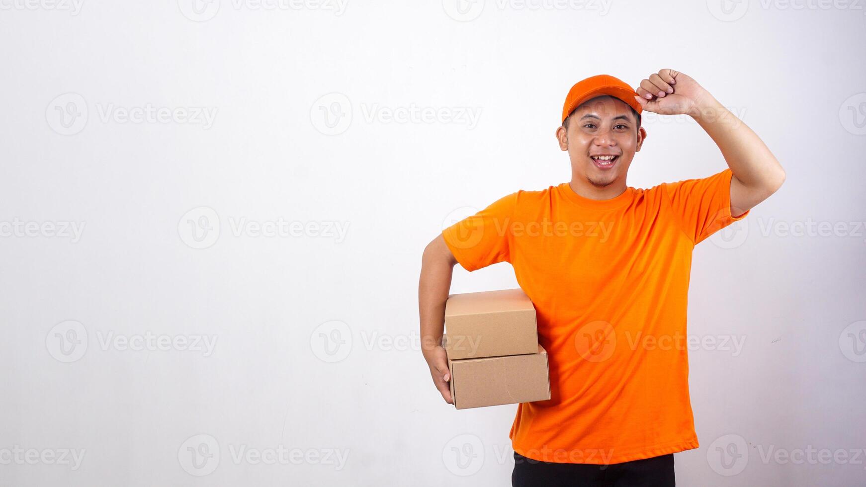 Asian deliveryman in orange t-shirt uniform carrying package boxes parcel and touching his cap visor isolated on white background photo