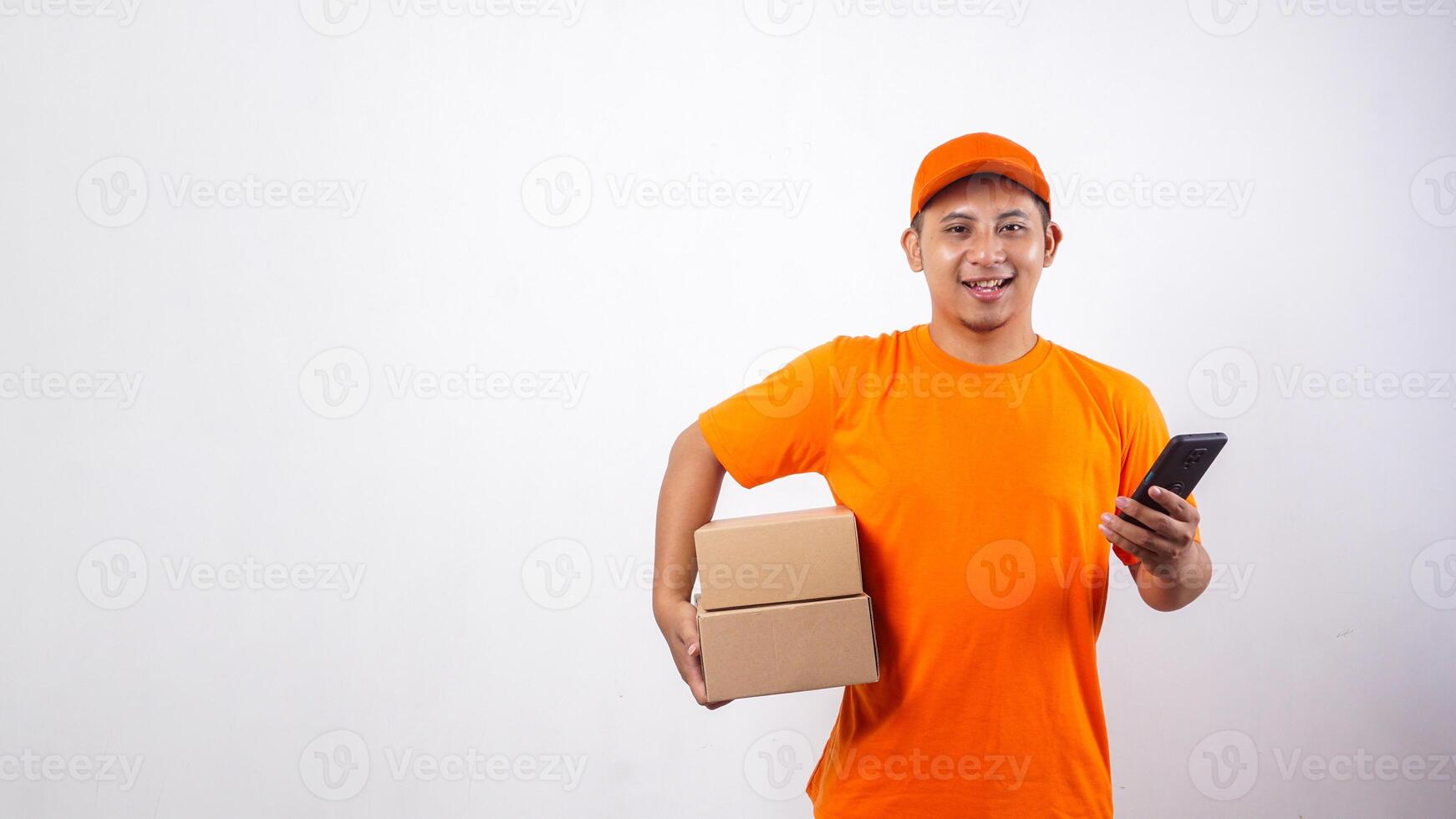 Asian Delivery man in orange t-shirt carrying package boxes parcel while holding a smartphone isolated on white background photo